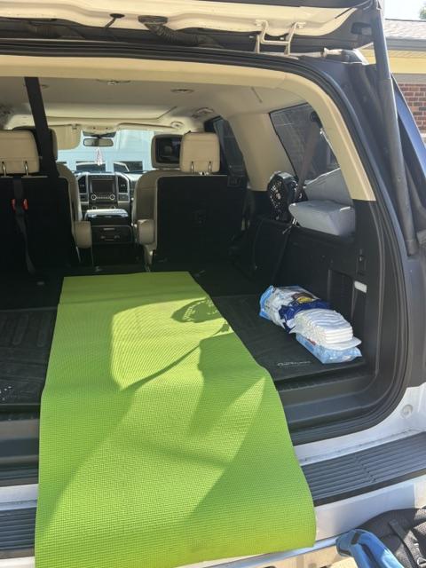 A lime green yoga mat lies in the trunk of a Ford Expedition MAX next to a stack of diapers and wipes that serves as a makeshift changing station.